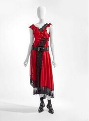 A. Japon in de vorm van onderjurk, een in rode tricot met daarlangs een strook zwarte machinale ka...