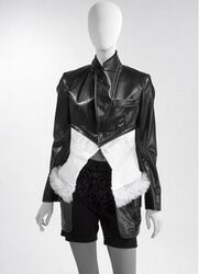 A. Jas in zwart imitatie leder en wit katoen dat een ingezet stuk vormt; in de katoen een strook g...