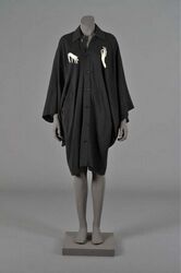 Lange zwarte bloeze met opgezette kraag en kimonomouwen; sluiting met zeven zwarte knopen in kunst...